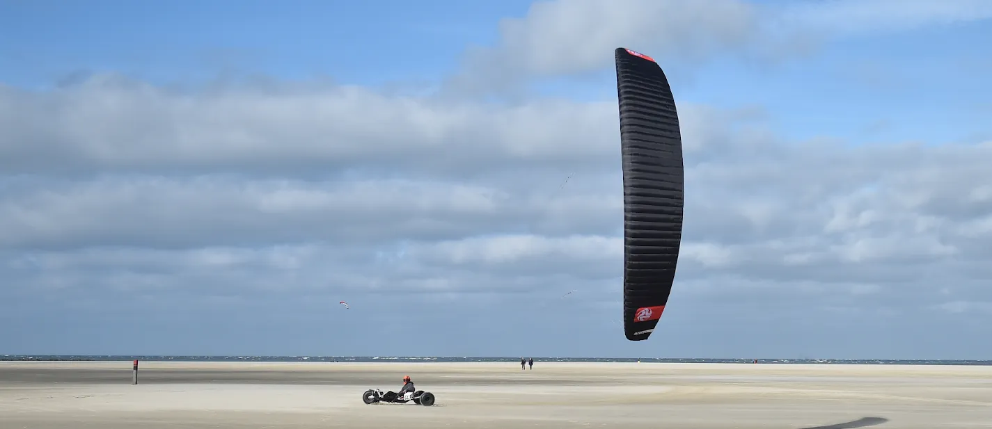 Kitebuggy met zwarte kite op het brede strand van Texel