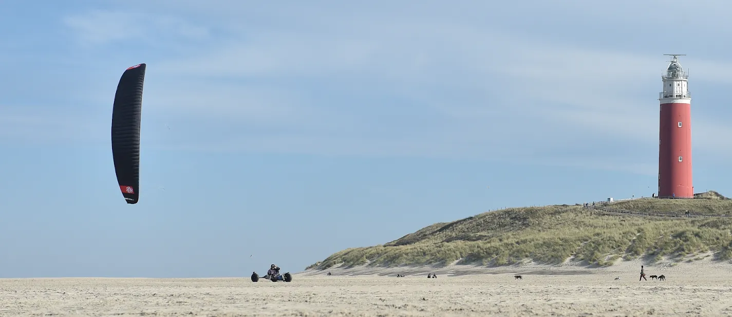 Kitebuggy met zwarte kite, rechts de rode vuurtoren van Texel op het duin
