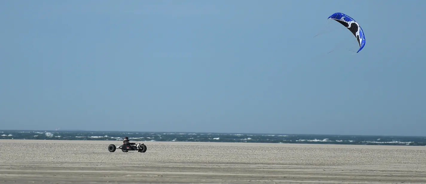 Kitebuggy met blauwe kite langs de waterlijn