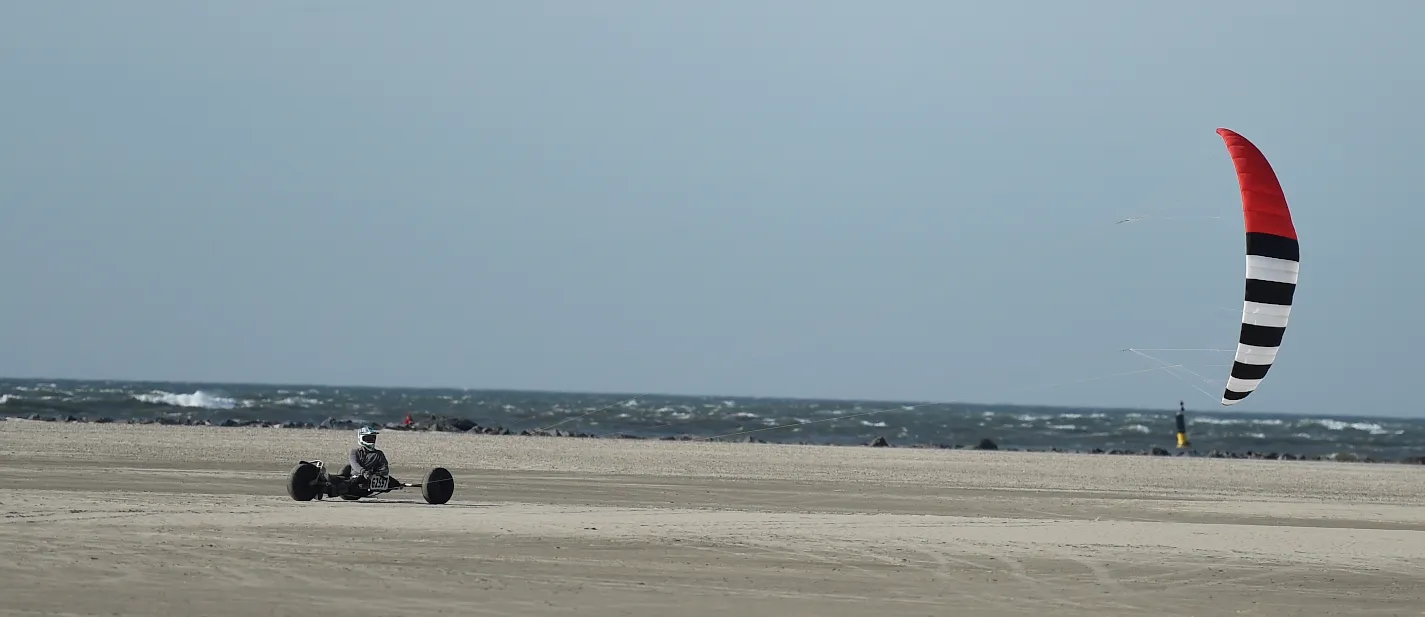 Kitebuggy met rood-wit gestreepte kite op het strand