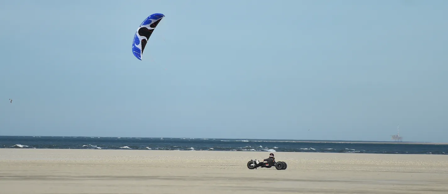 Kitebuggy met blauwe kite voor de zee