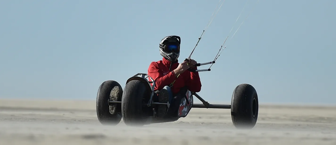 Kitebuggyrijder in rode jas rijdt op de camera af